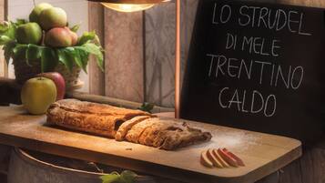 A loaf of bread on a wooden board, a basket of apples, and a sign with Italian text.