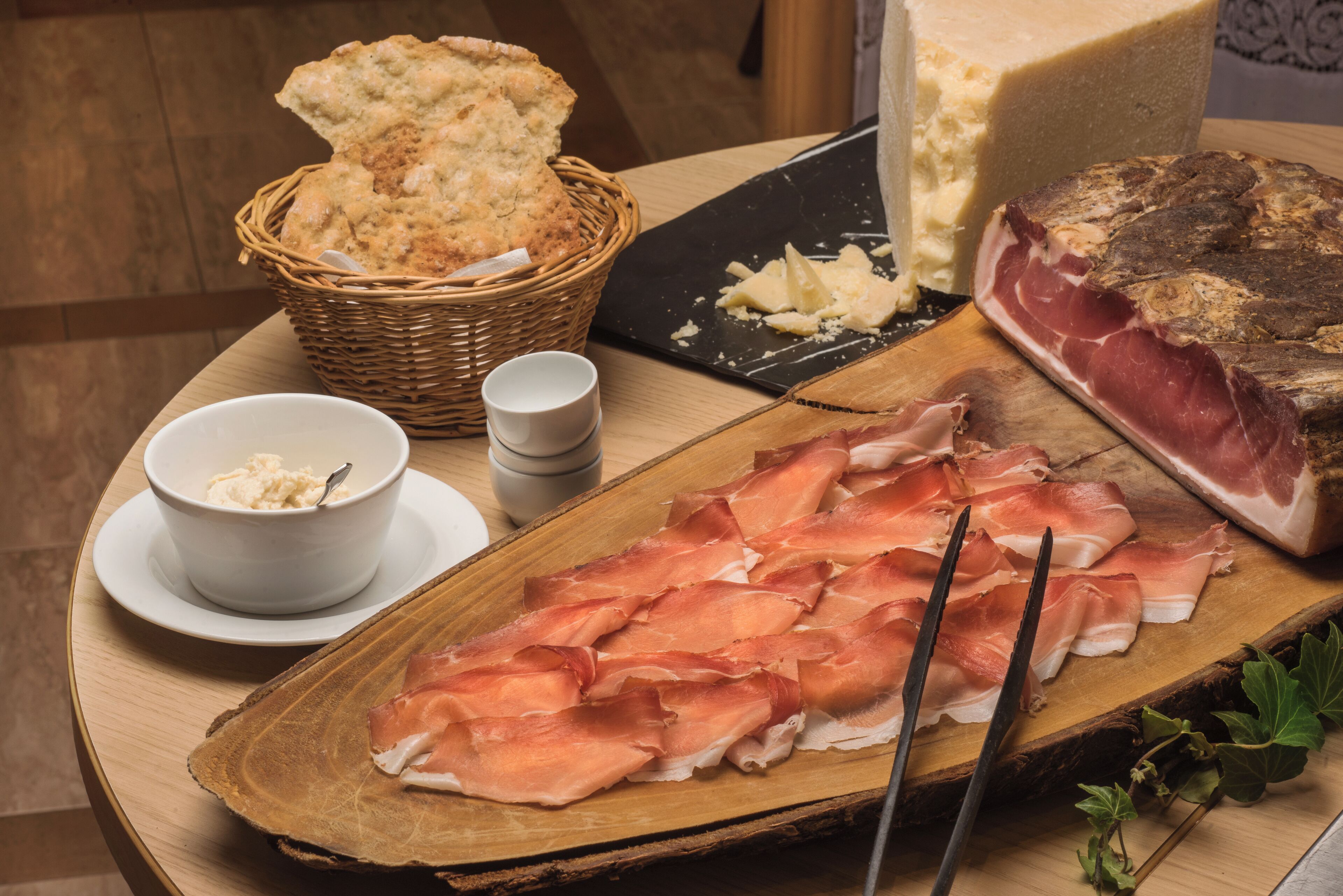Una tabla de embutidos con jamón serrano en lonchas, queso y galletas sobre una tabla de madera.