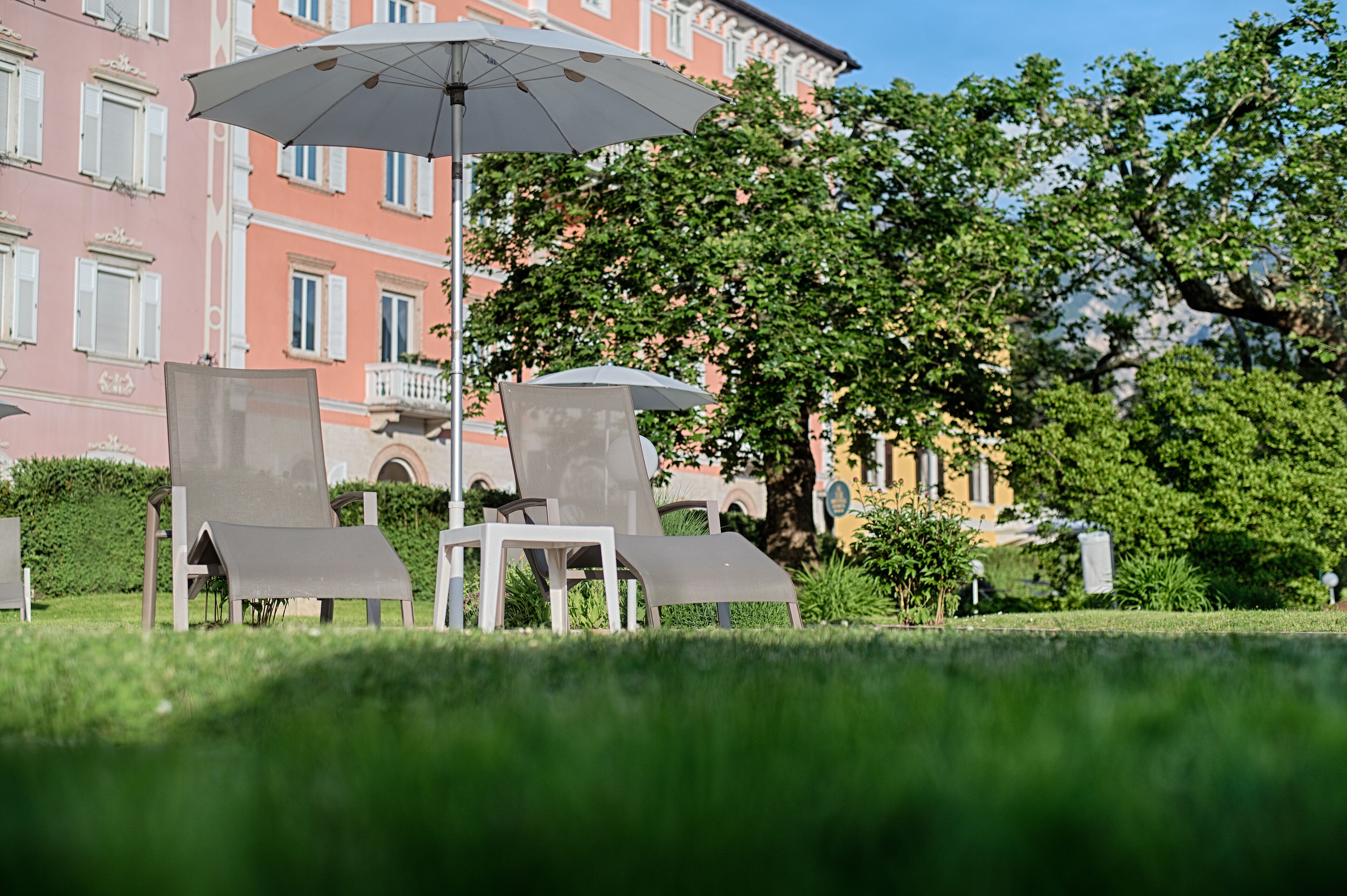 Outdoor seating with umbrellas, a grassy area, and a building with balconies in the background.