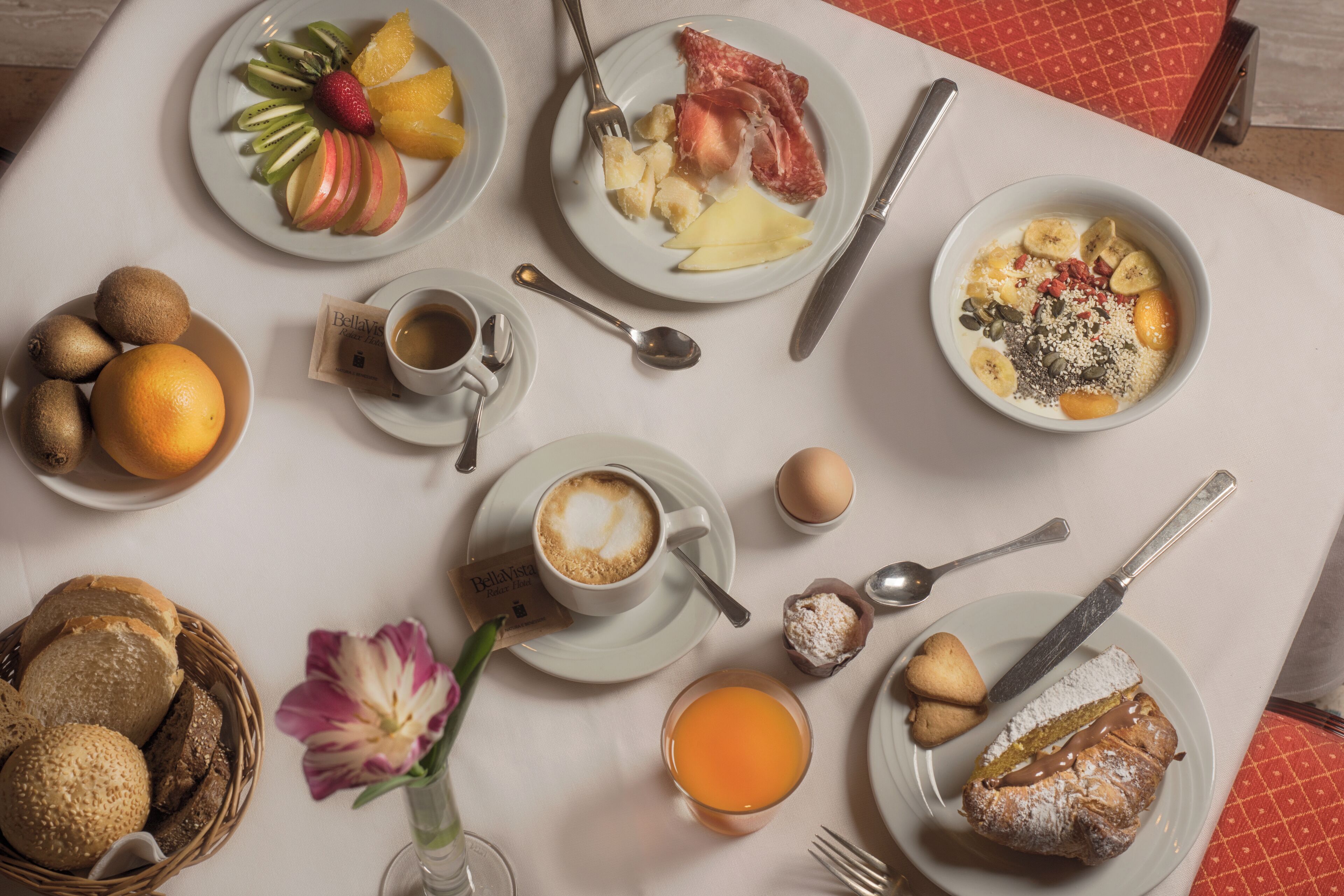 A breakfast table with various food items, a cup of coffee, and a flower.