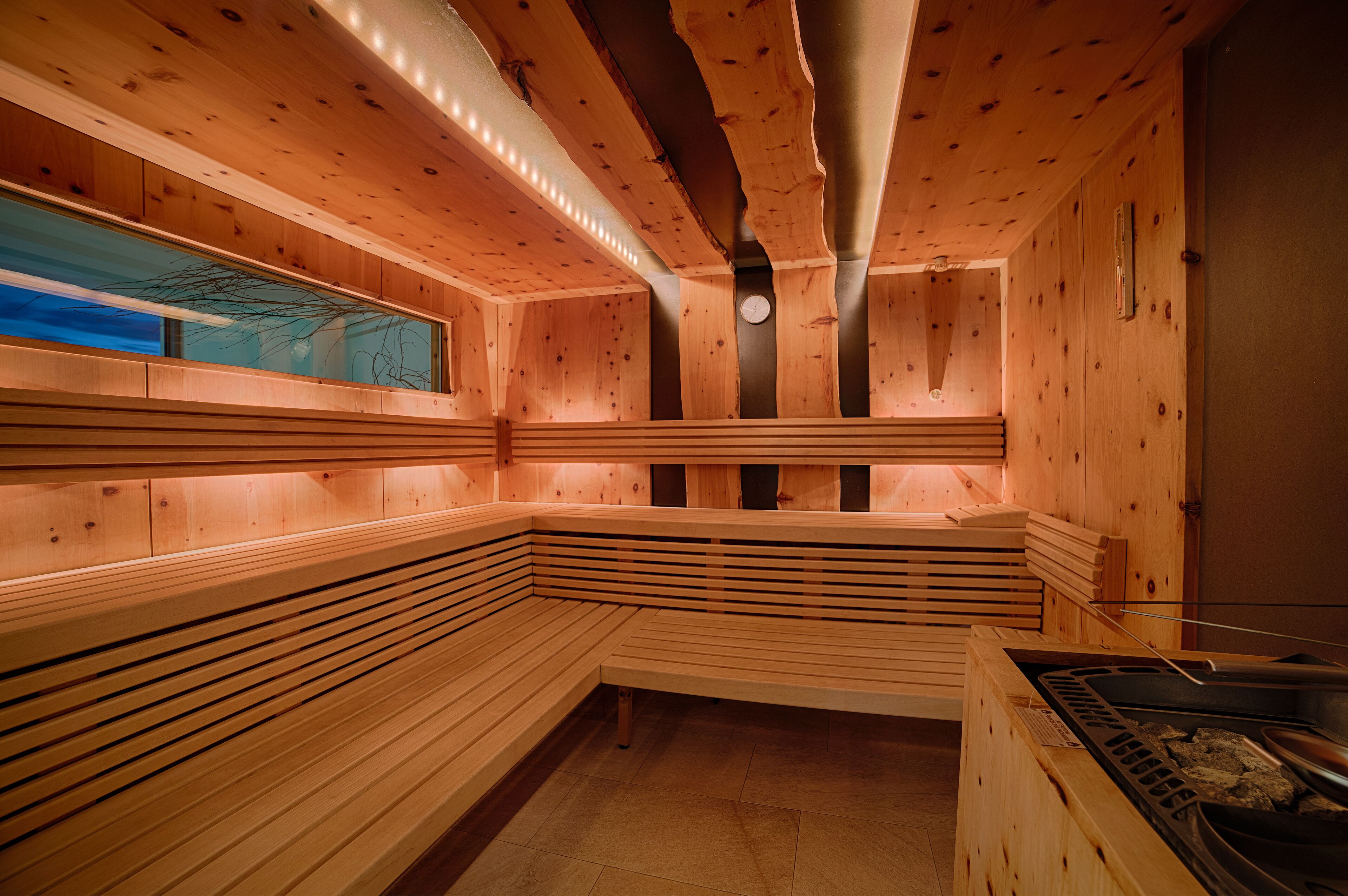 Una sauna con bancos de madera, un calentador a la vista y un ventanal con vistas a árboles.