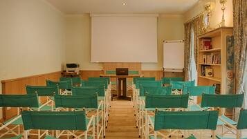 Une salle de conférence avec des rangées de chaises vertes, un écran de projection blanc, un pupitre en bois et une bibliothèque contenant des livres et des objets décoratifs.