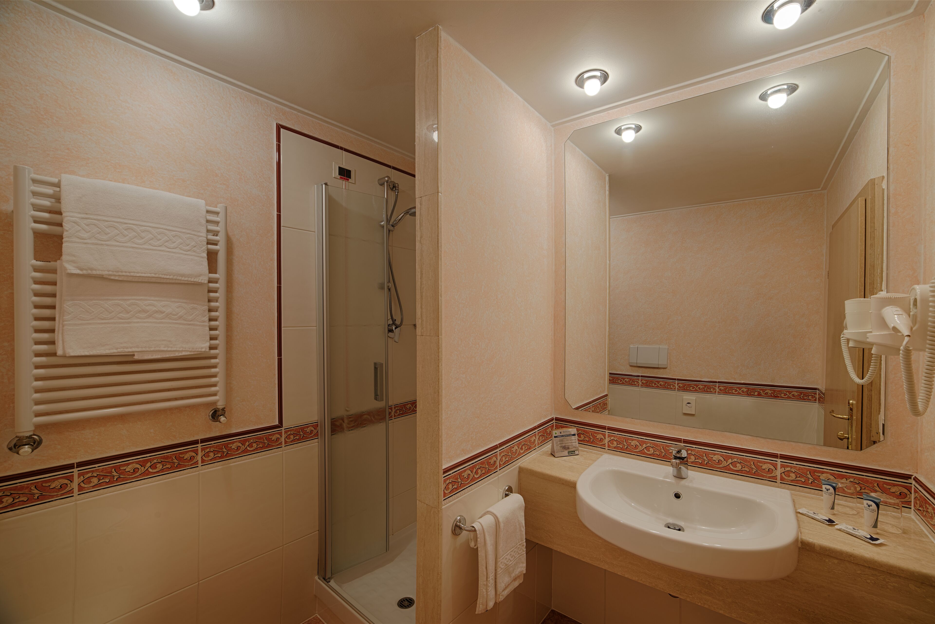 A bathroom with a glass-enclosed shower, a sink with a mirror, and a towel rack with folded towels.