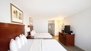 A hotel room with two beds, a desk with a TV, and a door leading to a hallway. - Seffner Inn and Suites (Seffner)