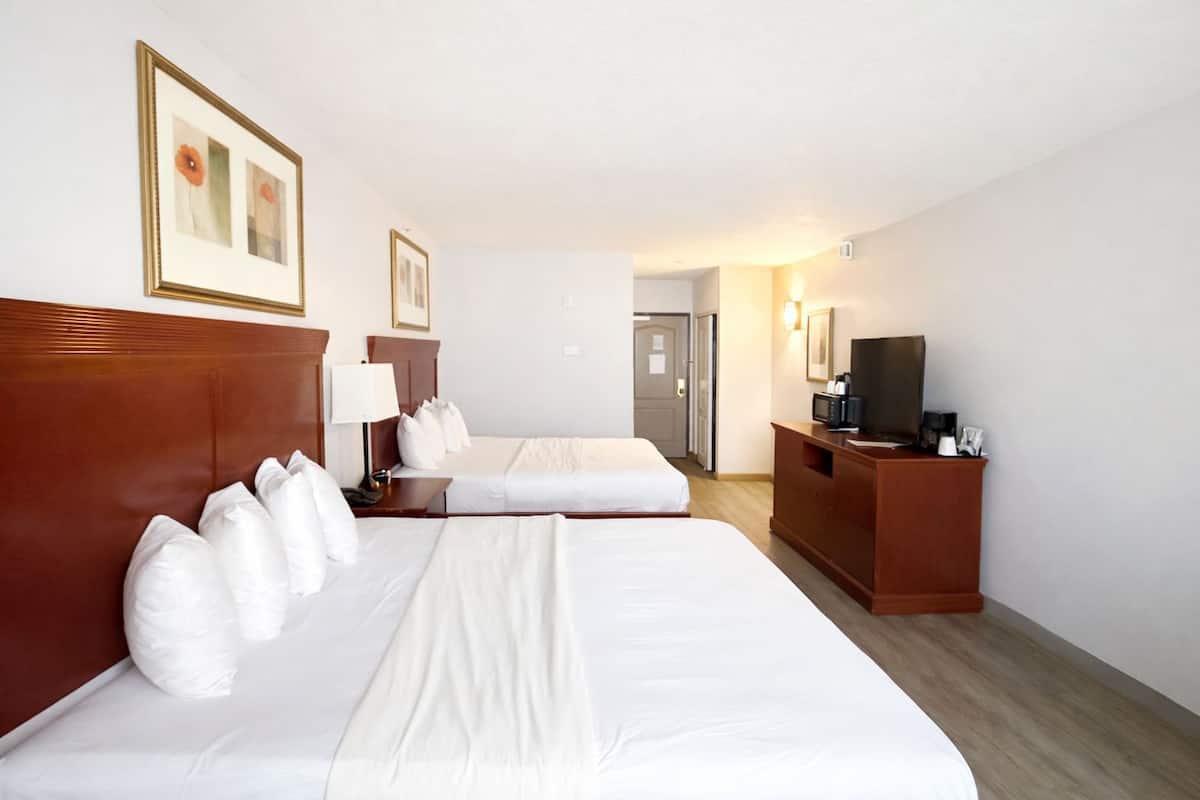 A hotel room with two beds, a desk with a TV, and a door leading to a hallway.