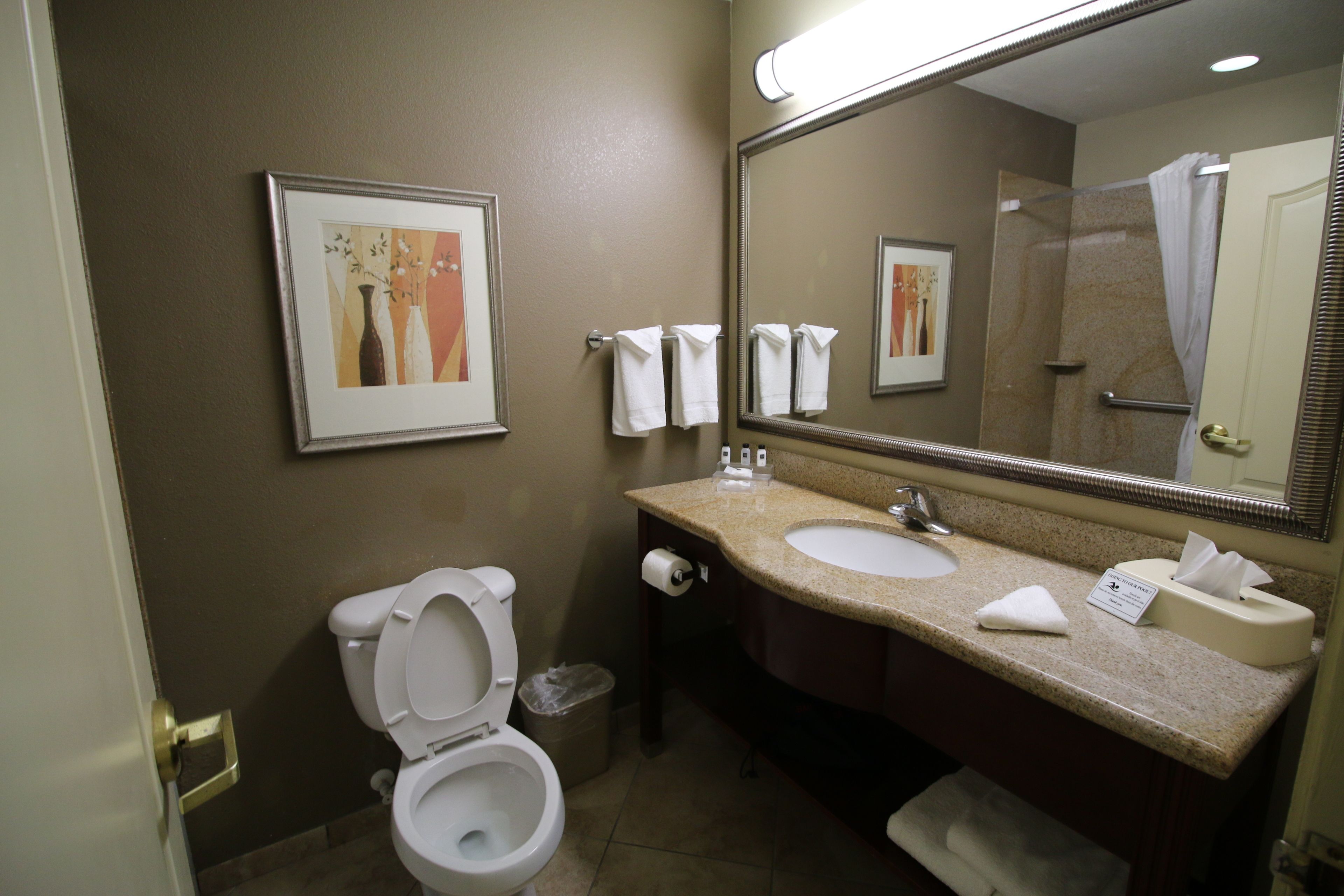 A bathroom with a toilet, sink, and mirror. There are towels hanging on the wall and a trash can.