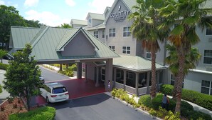 A hotel with a covered entrance, palm trees, and a red carpet leading to the parking area. - Seffner Inn and Suites (Seffner)