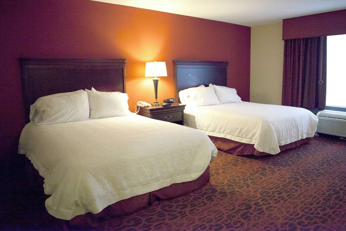 Una habitación de hotel con dos camas, una mesita de noche con lámpara y una ventana con cortinas.