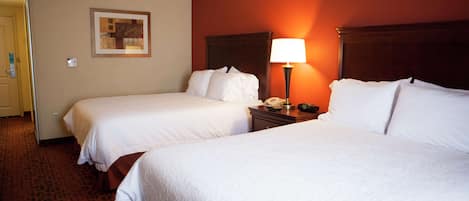 A hotel room with two beds, a nightstand with a lamp, and a framed picture on the wall.
