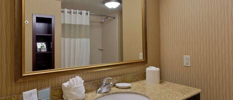 Baño de hotel con un espejo grande, un lavamanos y una zona de ducha.