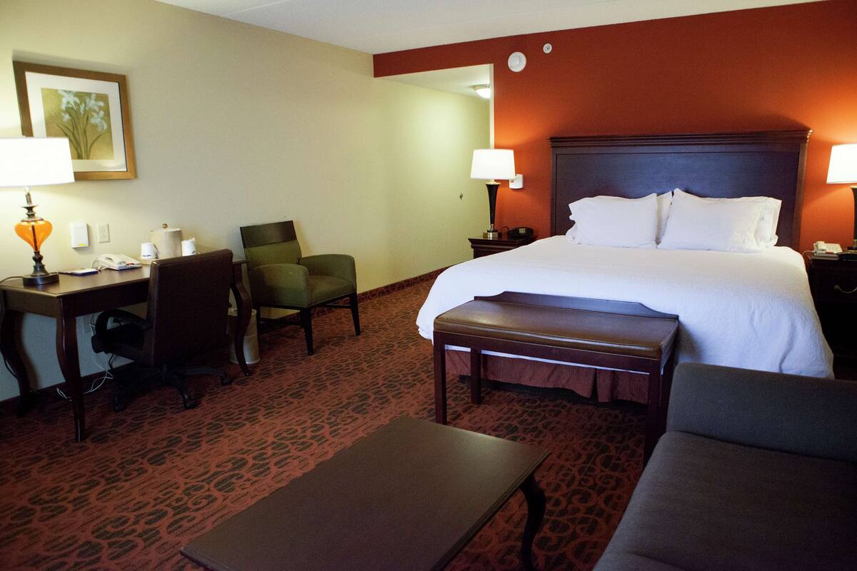Habitación de hotel con una cama grande, dos sillas, un escritorio con lámpara, teléfono y una mesita.