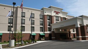 A Hampton Inn hotel with a clear entrance, American flags, and a parking sign.