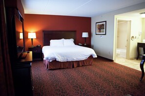 Habitación de hotel con una cama grande, dos mesitas de noche con lámparas, un cabecero de madera y una alfombra estampada.