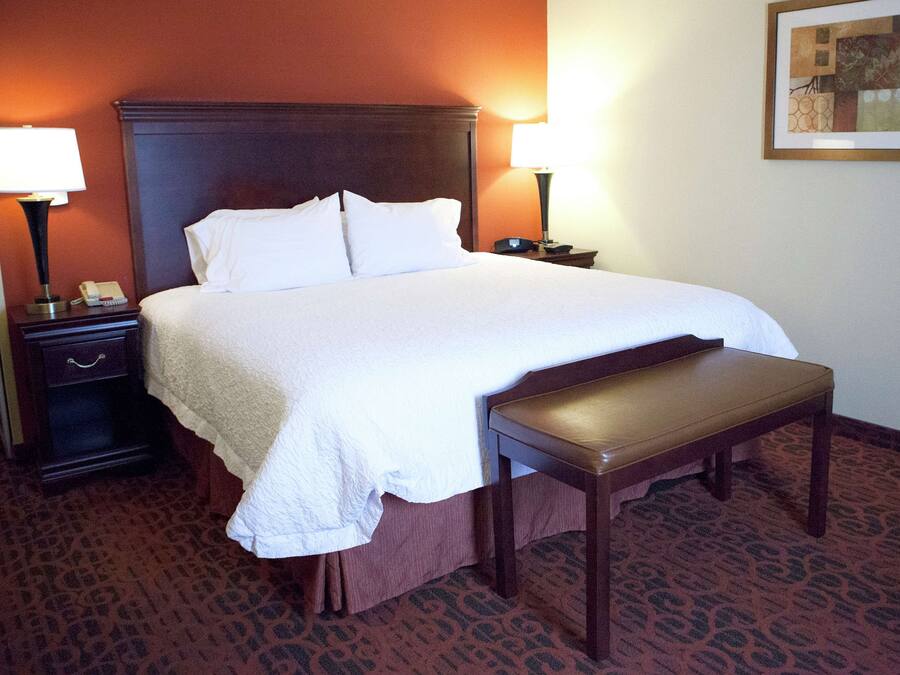 A hotel room with a large bed, two bedside tables with lamps, a bench, and a patterned carpet.