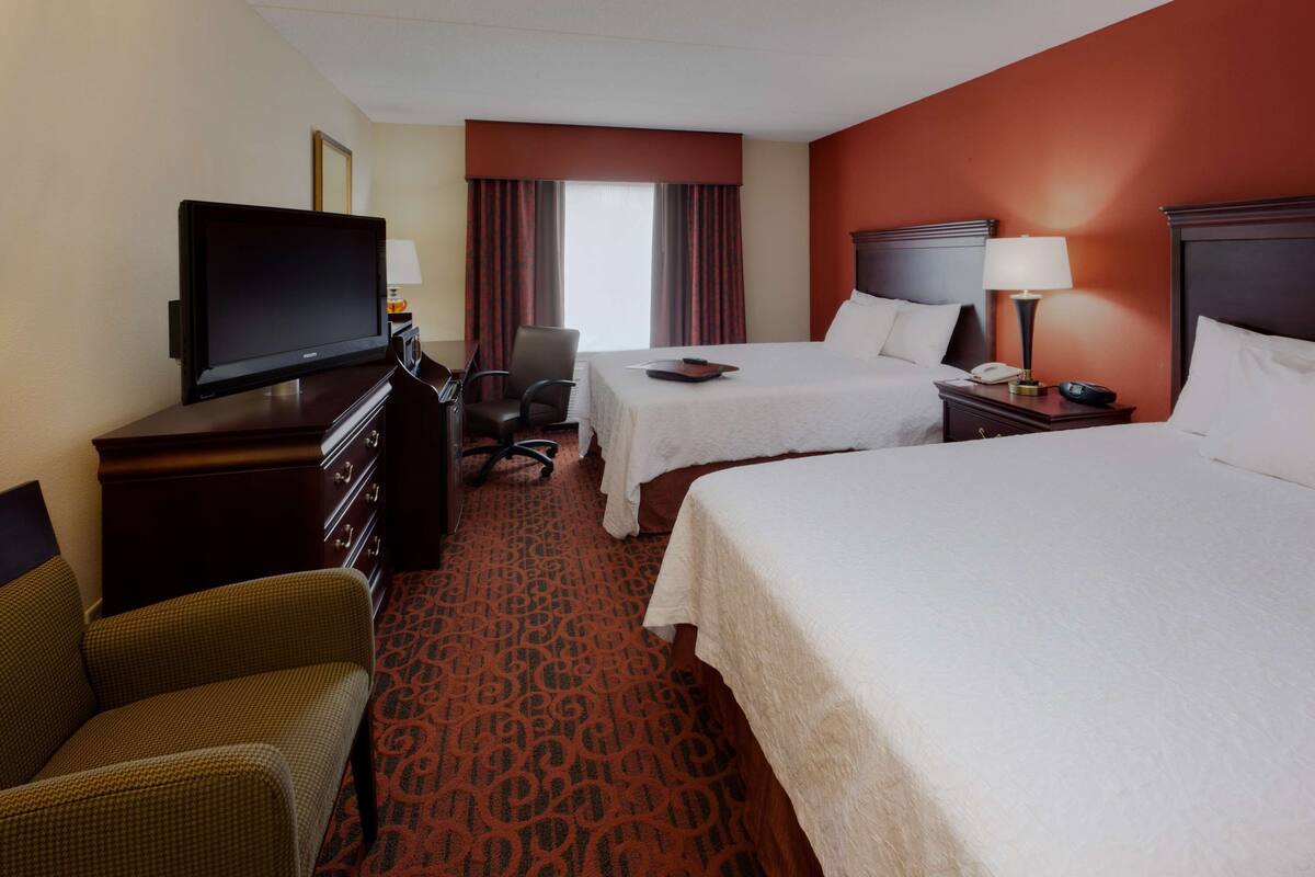 Habitación de hotel con dos camas, televisión, escritorio con computadora, una silla y alfombra estampada.