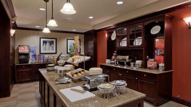 A hotel kitchen with a buffet setup, including a variety of food items and a coffee station. - Hampton Inn Rochester Webster (Webster)