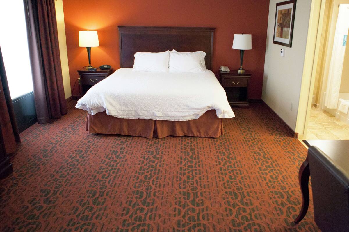 Habitación de hotel con una cama grande, dos mesitas de noche con lámparas, una alfombra estampada y un cabecero de madera.