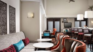 A hotel lobby with a sofa, chairs, a dining area, and a television. - Hampton Inn & Suites Chicago Southland-Matteson (Matteson)