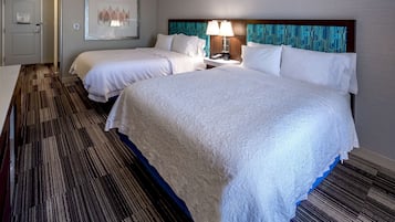 Camera d'albergo con due letti, un comodino con una lampada, un quadro appeso al muro e un tappeto a motivi.