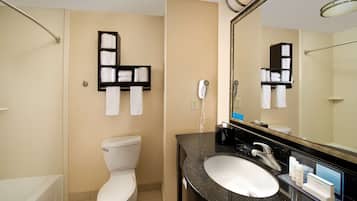 Un baño de hotel con inodoro, lavamanos y espejo. Hay toalleros en la pared y un secador de pelo.