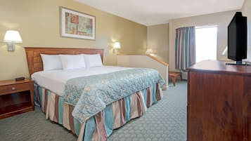 A hotel room with a large bed, bedside lamps, a desk, a television, and a window with curtains.