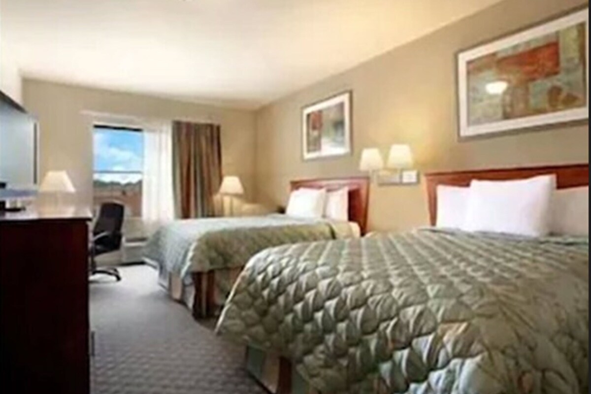 A hotel room with two beds, a desk, and a chair.