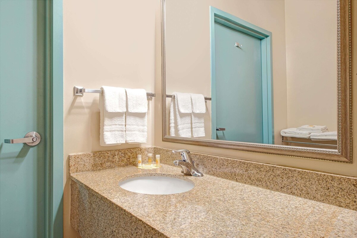A bathroom with a granite countertop, a white sink, a mirror, and a towel rack with folded towels.