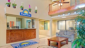 Eine Days Inn Lobby mit einer Rezeption, einem Sofa, einem Couchtisch und einem Balkon mit Holzgeländer.