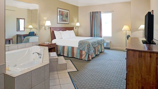 Ein Hotelzimmer mit einem großen Bett, einer Badewanne, einem Fernseher und einem Fenster mit Vorhängen.