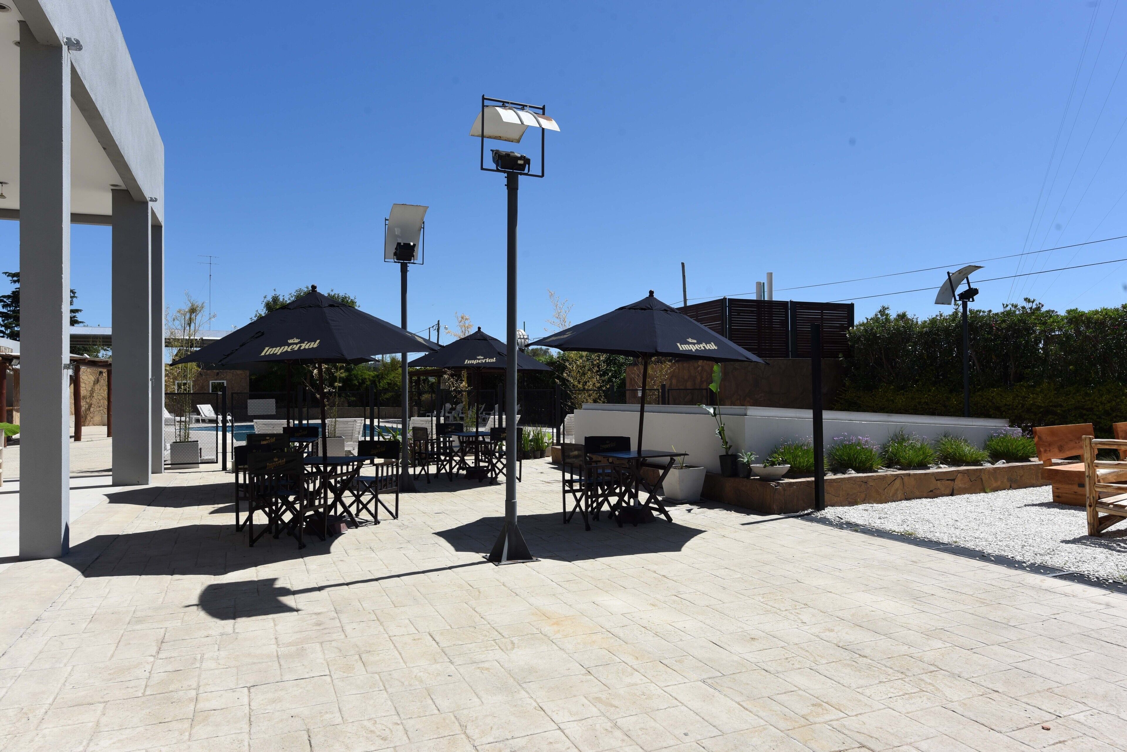 Un espace extérieur aménagé en terrasse, avec des tables et des chaises sous des parasols, une piscine et un bâtiment en arrière-plan.