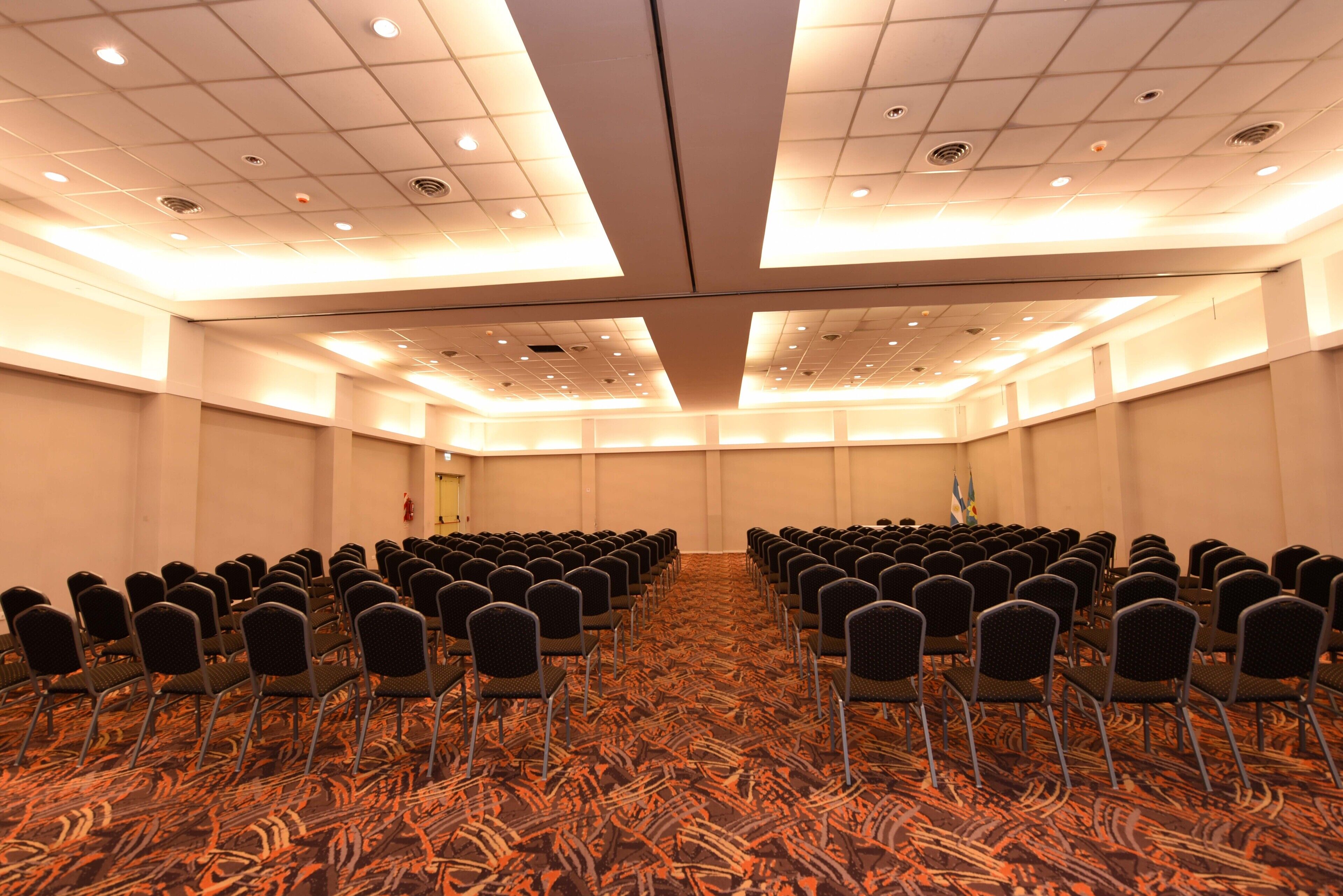 A conference room with rows of chairs, a patterned carpet, and a ceiling with recessed lighting.