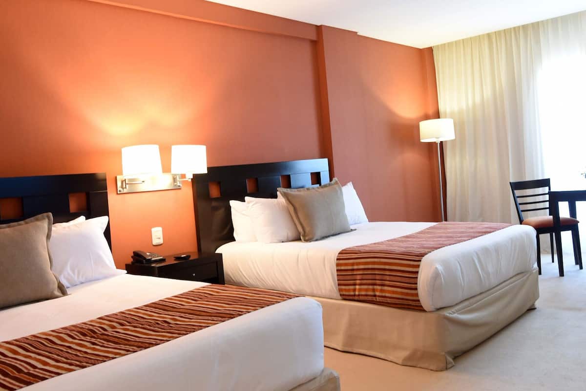 A hotel room with two beds, a desk, and a chair.