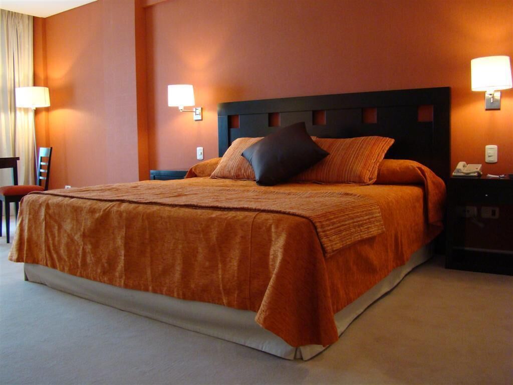 A large bed with a dark headboard, two bedside lamps, and a nightstand with a phone.