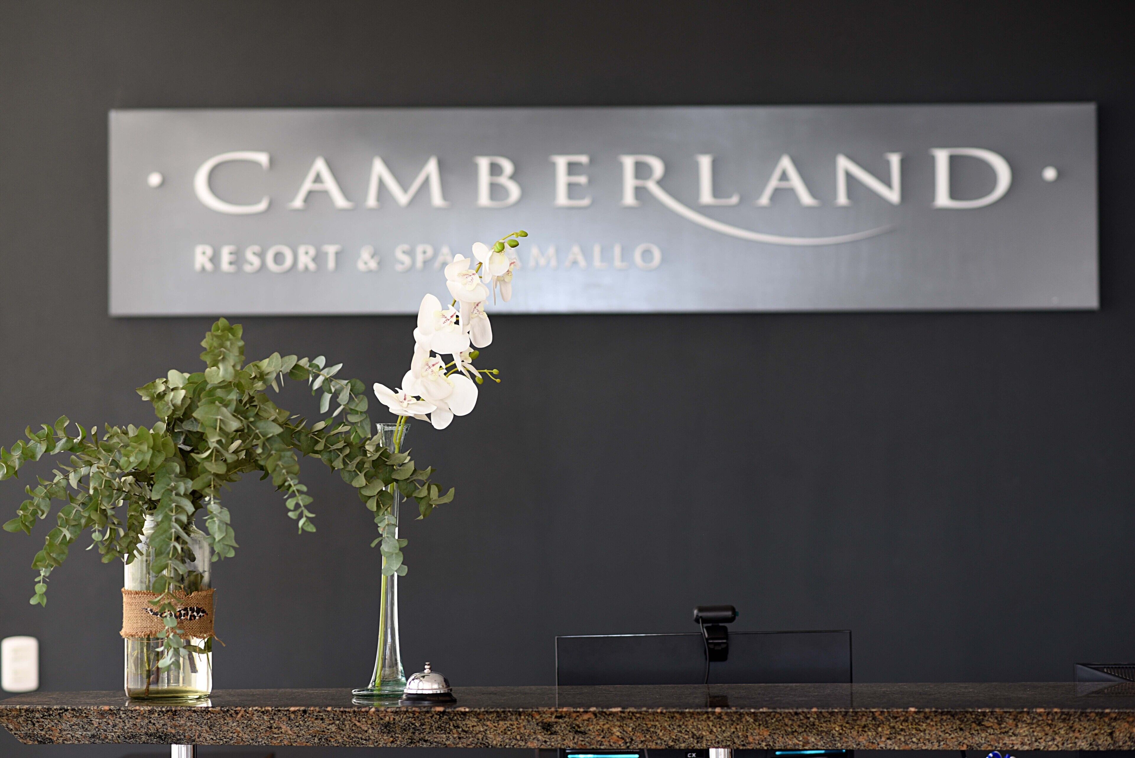 Un comptoir d’accueil avec une enseigne indiquant « Cumberland Resort & Spa Mallo » et deux vases ornés de fleurs.