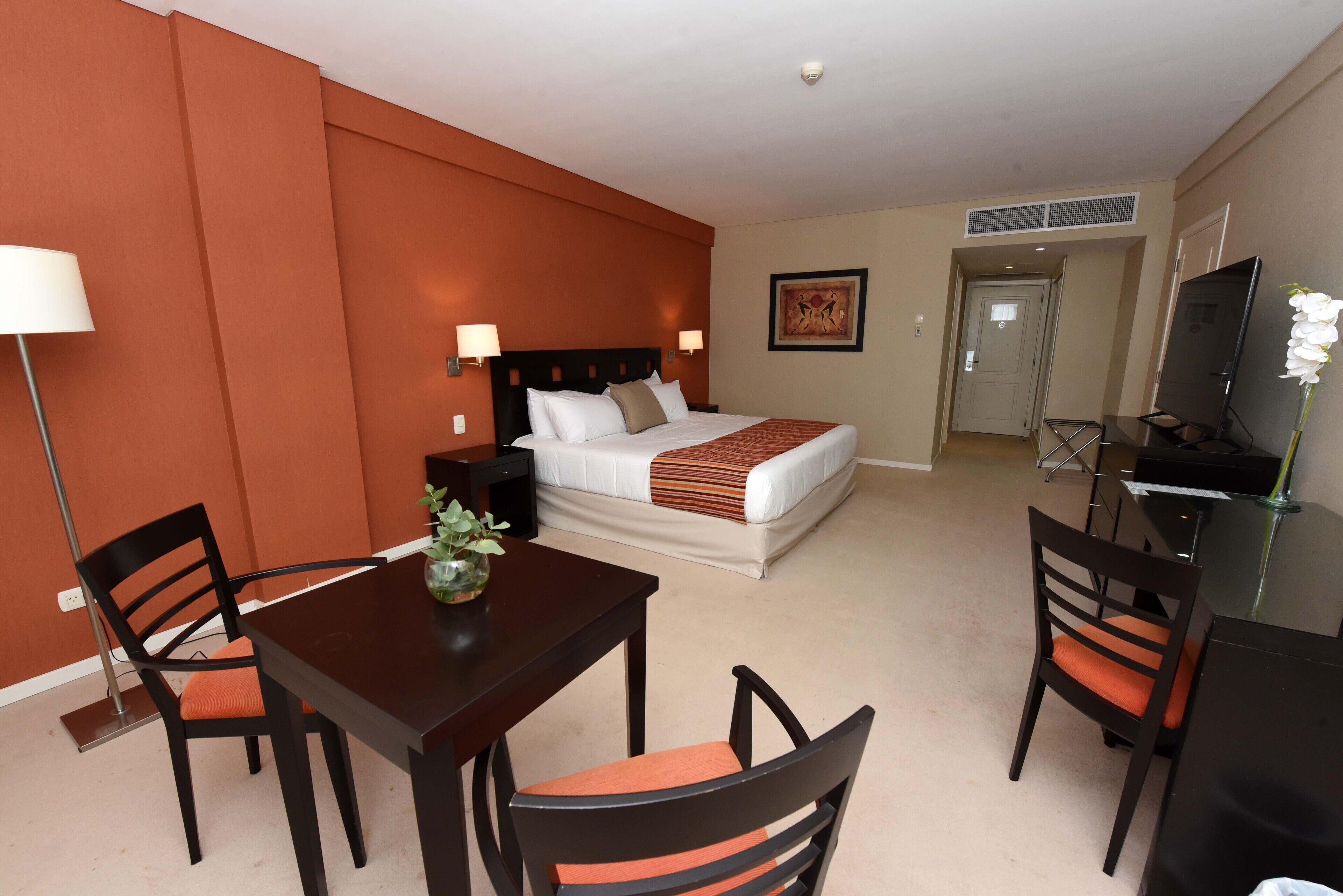Une chambre d’hôtel comprenant un lit, un bureau, deux chaises, une lampe et un téléviseur.