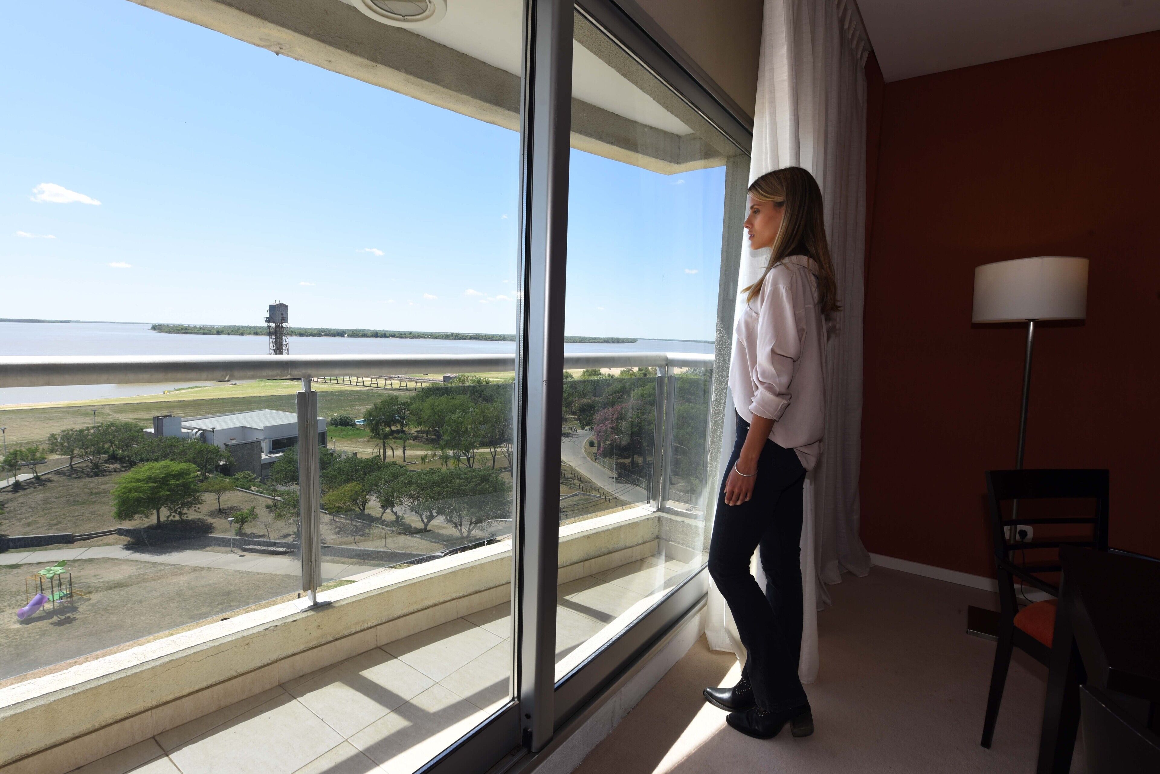 A room with a large window overlooking a park and a body of water.