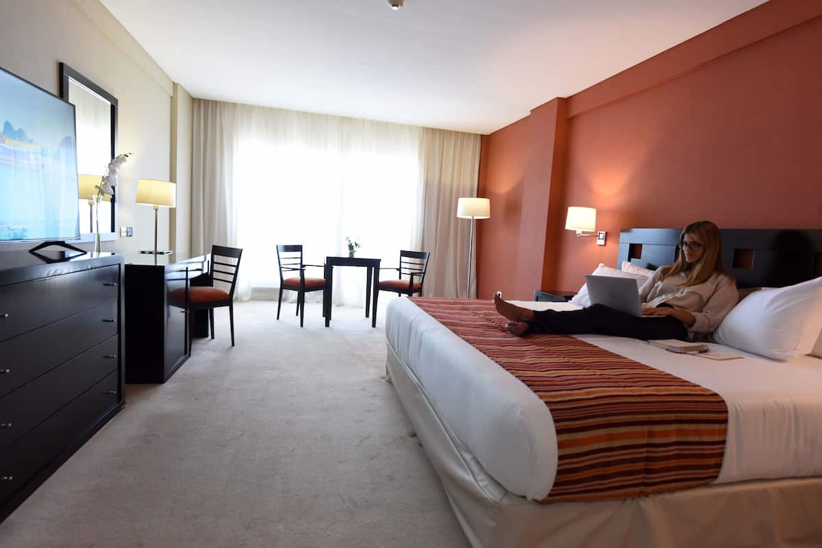 A hotel room with a bed, a desk, a chair, a TV, and a dresser.