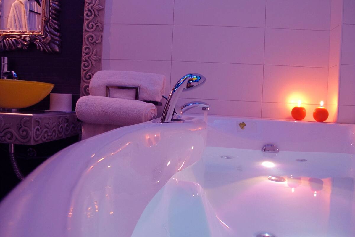 A bathroom with a bathtub, a yellow sink, a towel, and two lit candles.