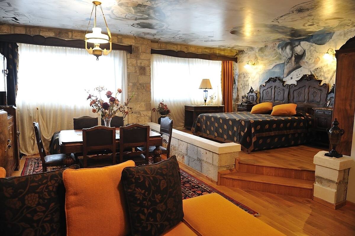 A room with a dining area, a bed with a polka dot bedspread, and a stone wall with a mural.