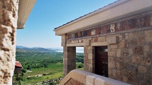 Un edificio de piedra con estilo arquitectónico clásico, que presenta una detallada franja decorativa y vistas a un paisaje verde con montañas al fondo.