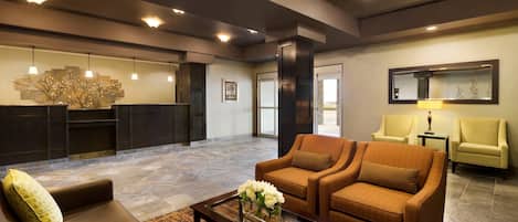 A lobby with a reception desk, two sofas, a coffee table with flowers, and a mirror on the wall.