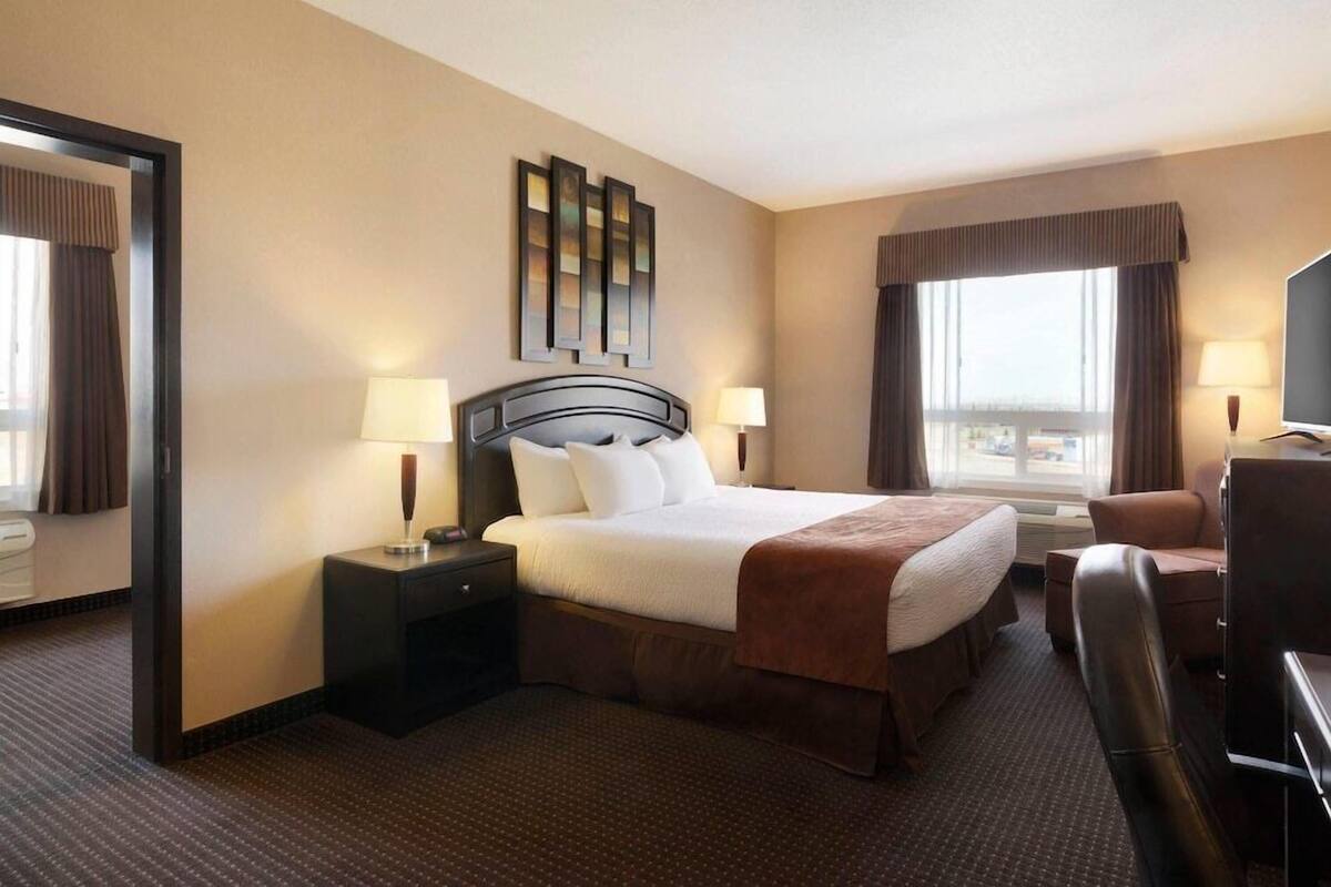 A hotel room with a bed, two bedside tables, a chair, a TV, and a window with curtains.