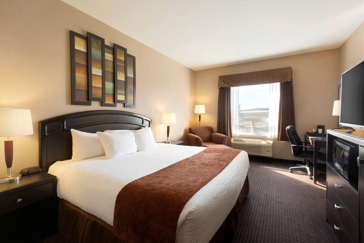 A hotel room with a bed, bedside lamps, a desk with a chair, a television, and a window with curtains.
