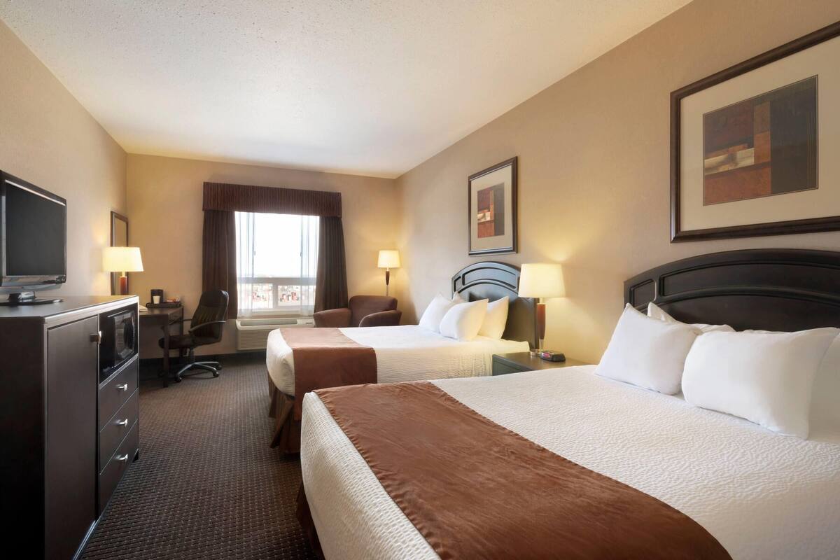 A hotel room with two beds, a desk, a chair, a television, and a window with curtains.