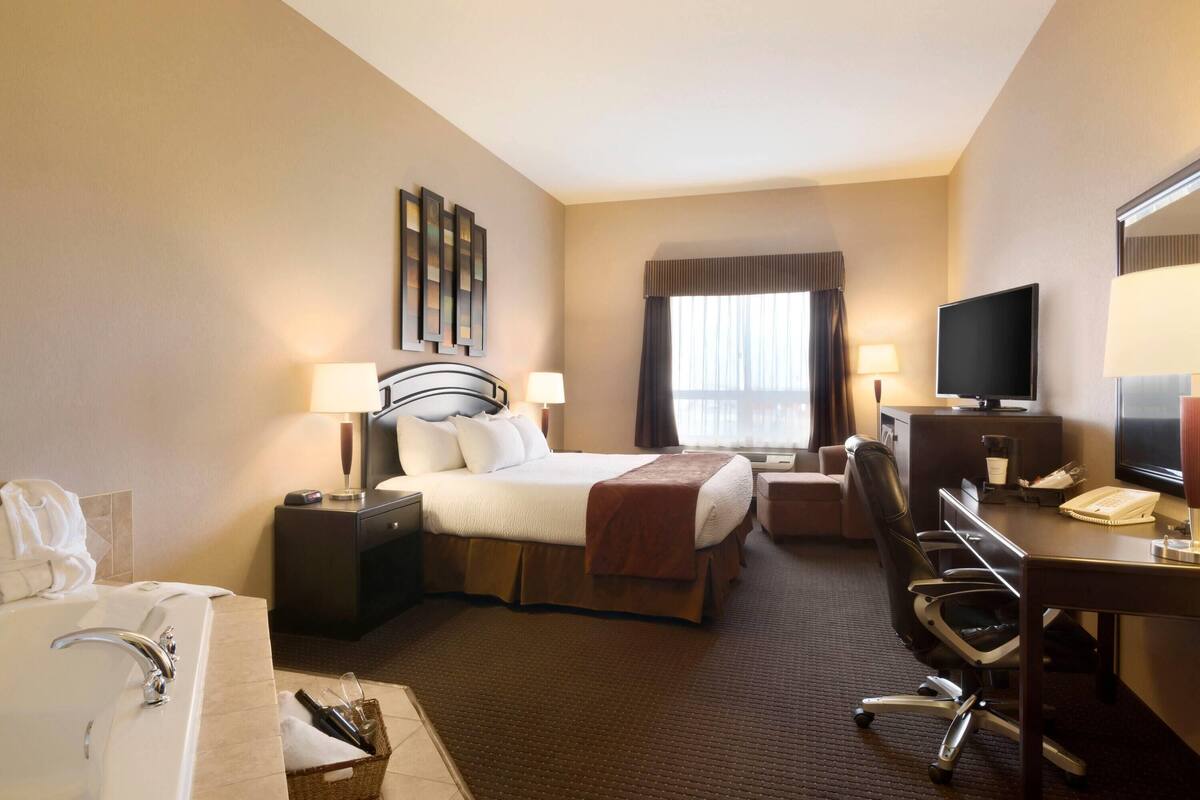 A hotel room with a bed, desk, chair, television, and a window with curtains.