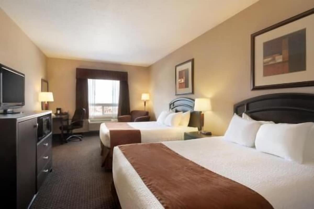 A hotel room with two beds, a desk, a television, and a window with curtains.