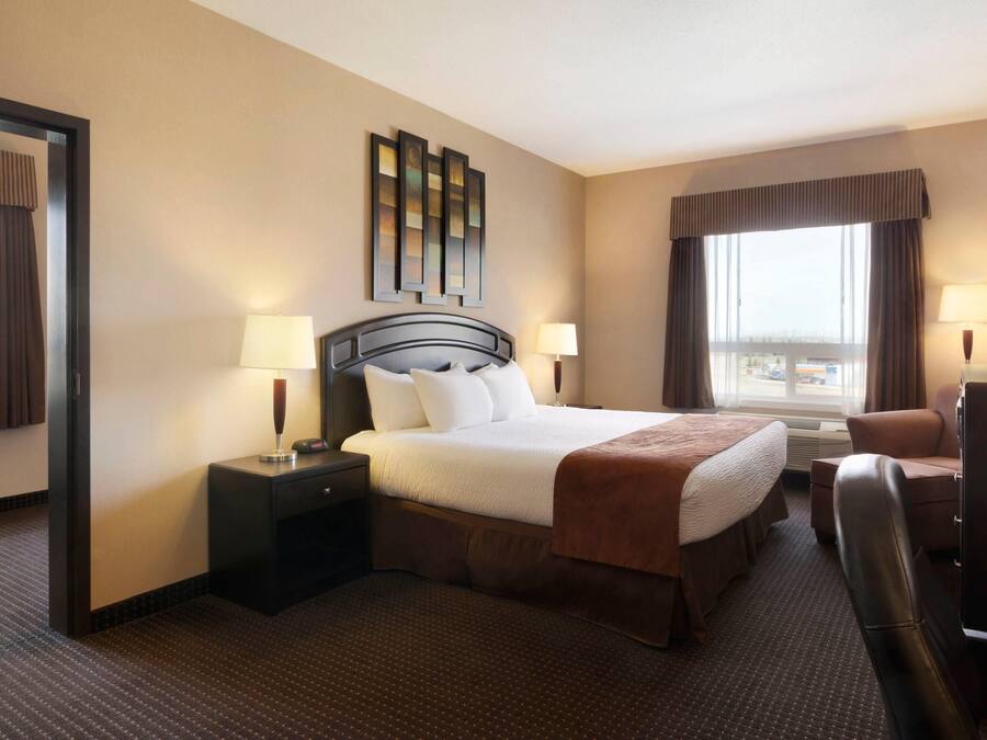 Habitación de hotel con cama, dos mesitas de noche, un escritorio con silla, un ventanal grande y televisor montado en la pared.