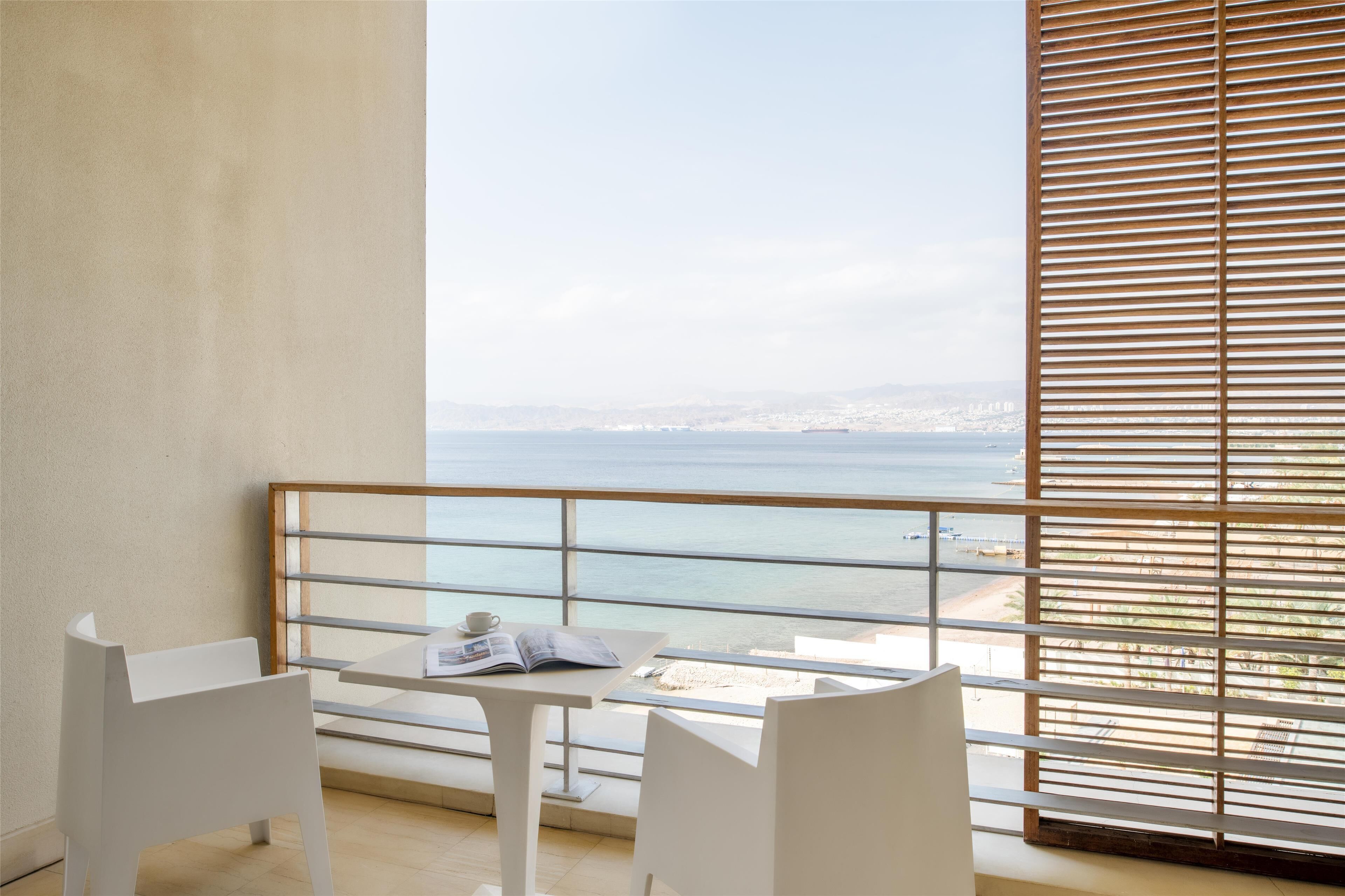 Varanda com mesa e cadeiras, vista para o litoral e guarda-corpo.