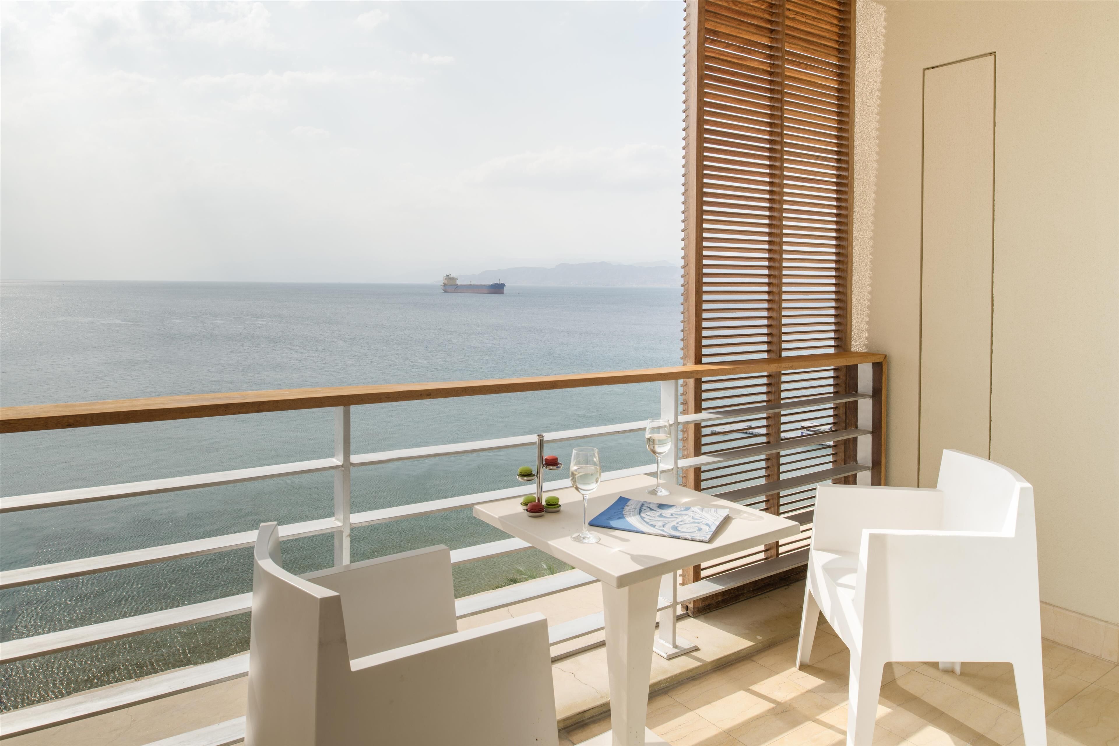 A balcony with a table, two chairs, and a view of the sea.