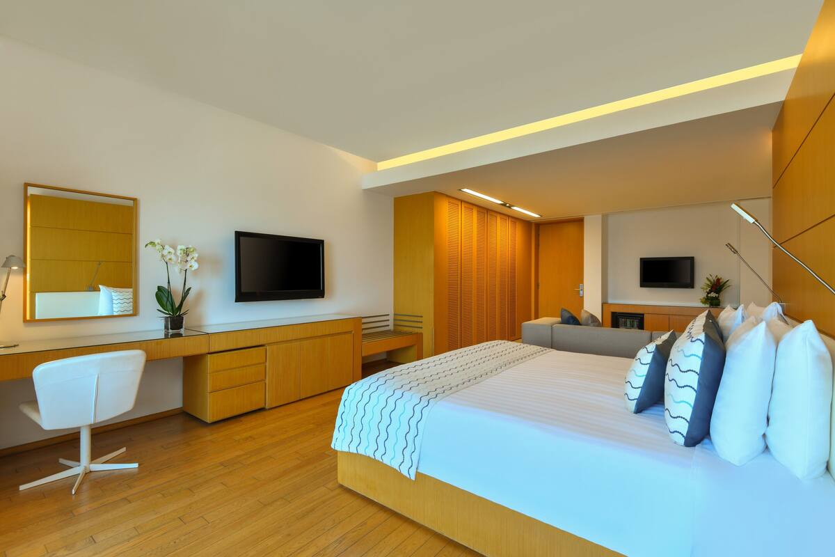 A modern bedroom with a large bed, a desk, a chair, and two TVs.